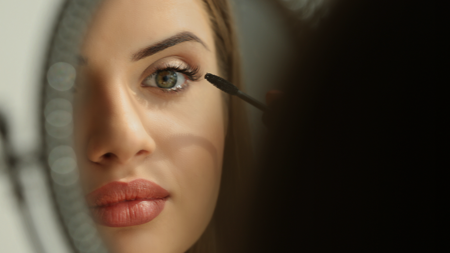 Woman applying eyeliner her face with a neutral background