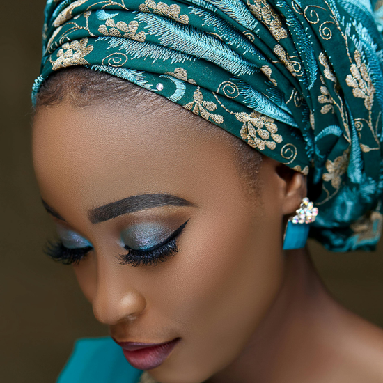 Woman wearing a teal headscarf with gold patterns, looking downward.