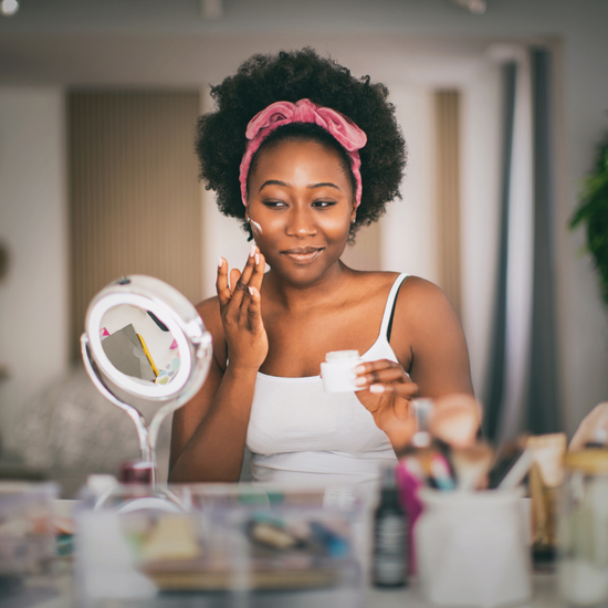 Woman applying cream to her face in front of a mirror