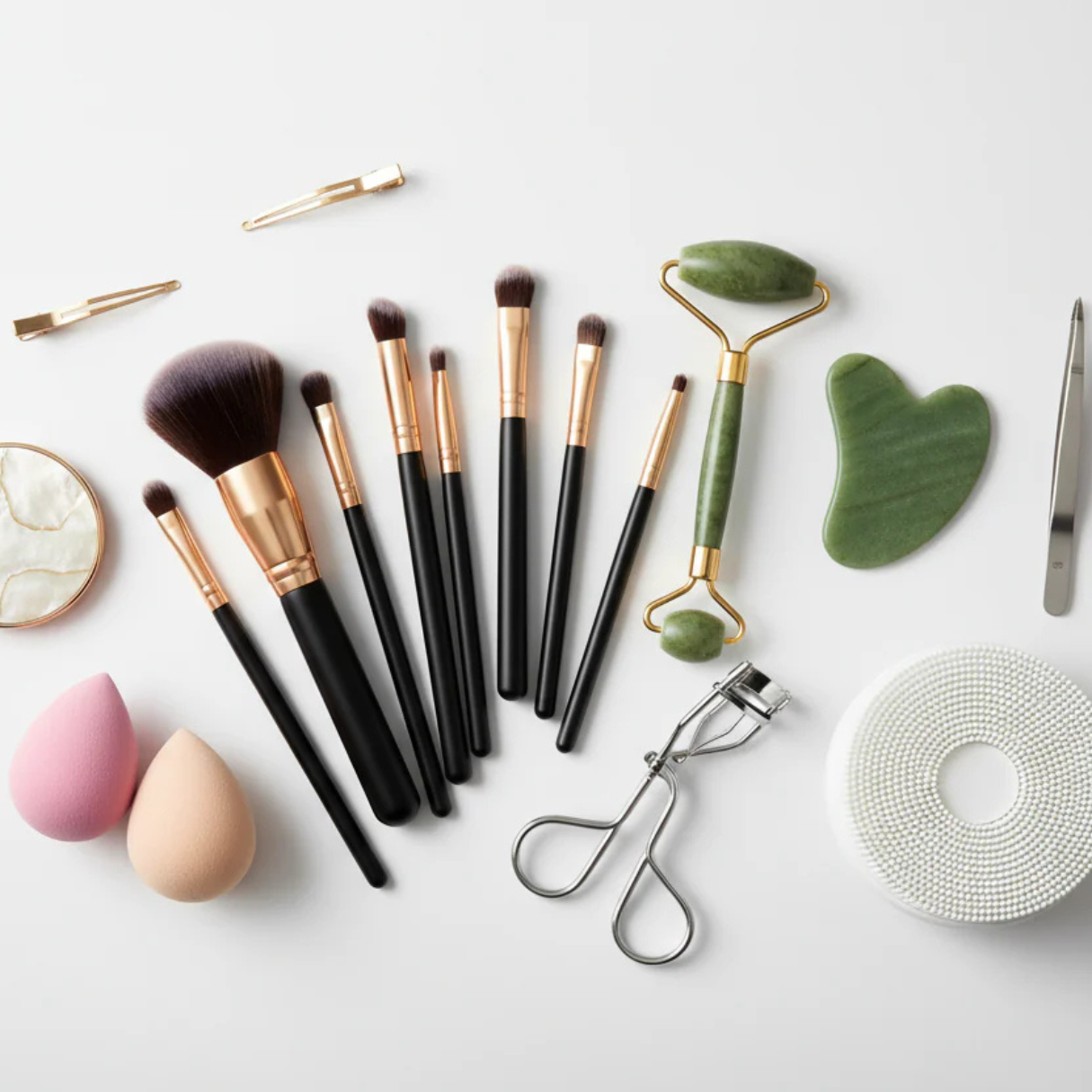 Collection of makeup brushes, skincare tools, and accessories on a light gray background