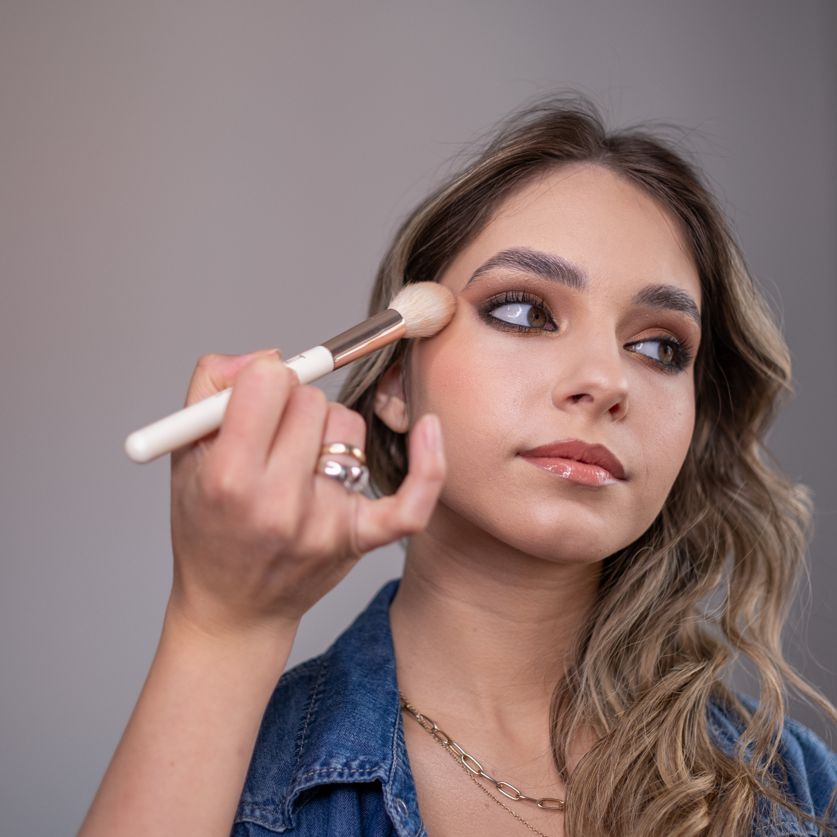 Woman applying makeup with a brush on a neutral background