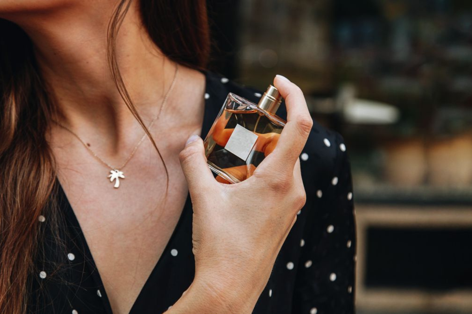 Woman spraying fragrance on wrist, enjoying perfume scent.