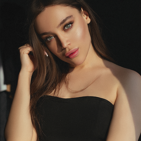 Woman with long brown hair wearing a black strapless top against a dark background
